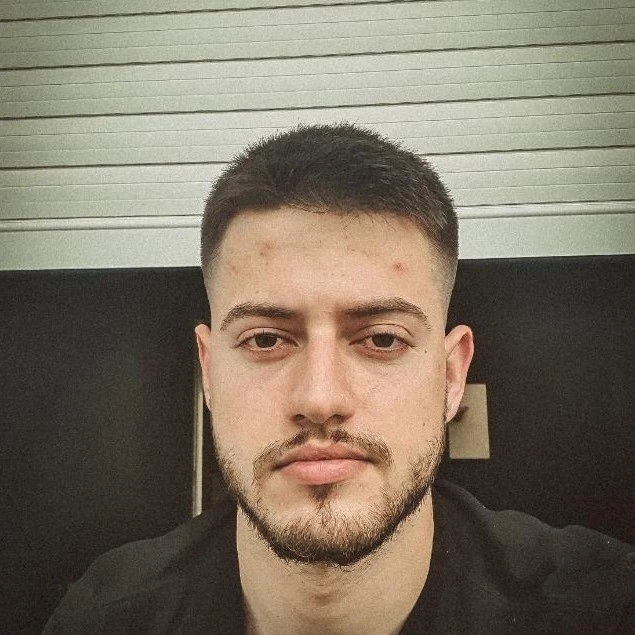 A man with a beard, showcasing his facial hair prominently. It appears to be a portrait taken indoors, highlighting his features such as the forehead, eyebrows, and chin. The background seems to consist of a wall, adding depth to the selfie-style photograph.